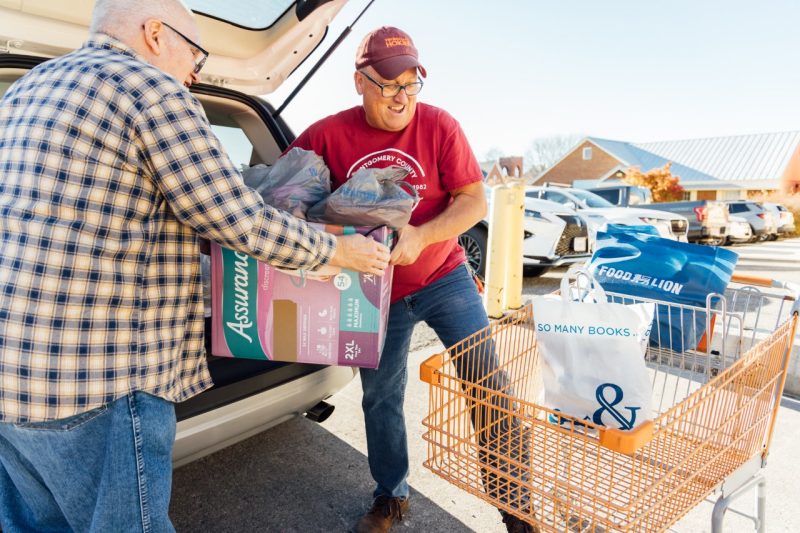 John Tarter hefts boxes and bags of donations from an open car trunk into an orange shopping cart.