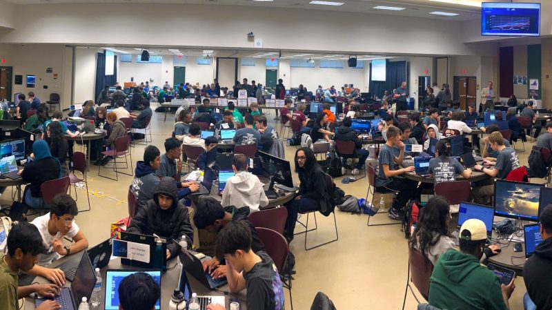 a large room full of students work on laptops to solve cybersecurity challenges.