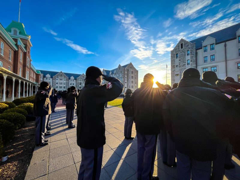 Cadets standing in a group in uniform salute as the sun shines through their group