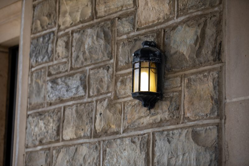 An exterior lantern style light on a grey Hokie Stone wall of a building near a doorway